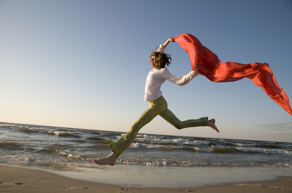 woman jumping on beach with fabric